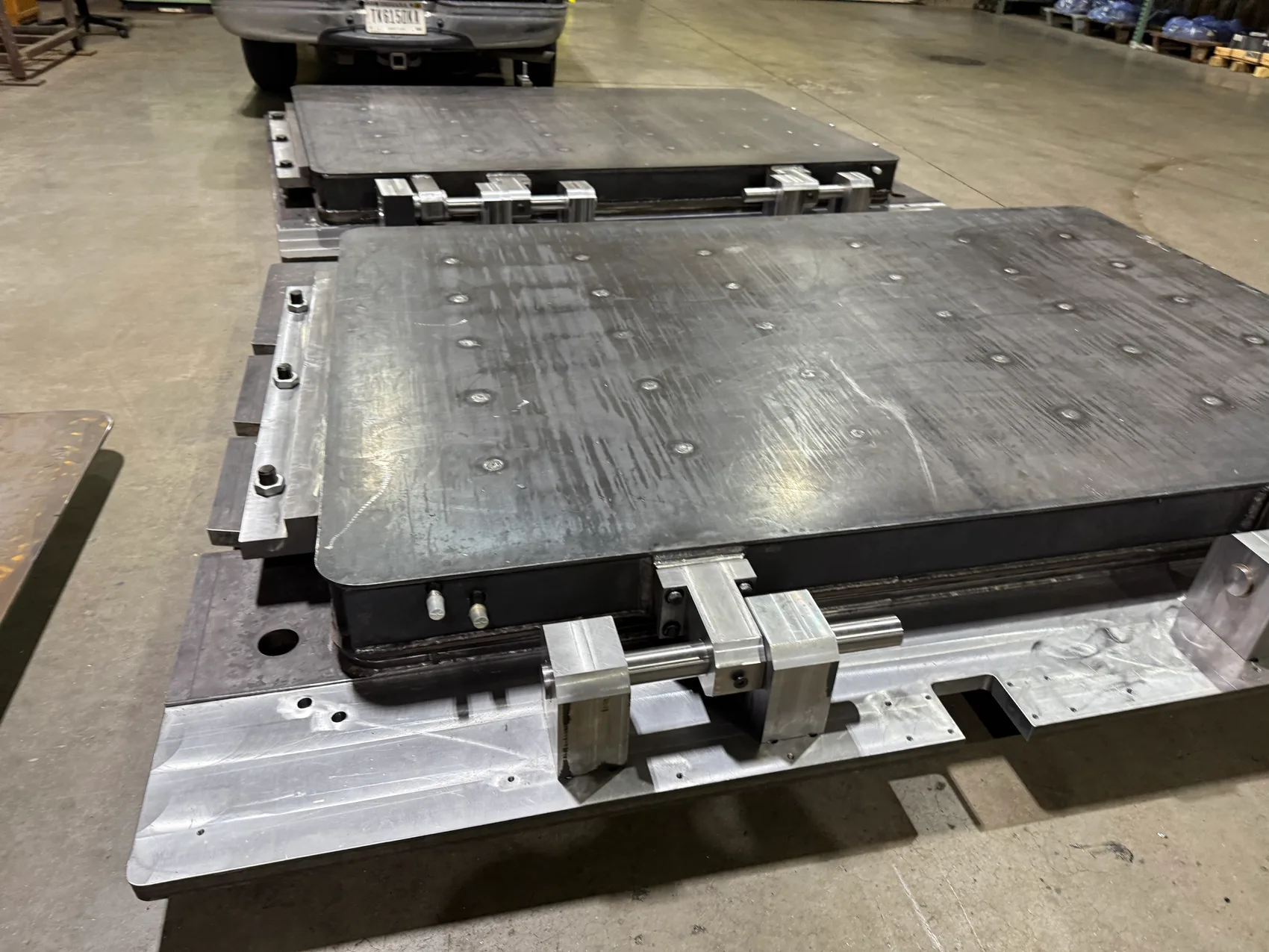 Two finished black steel 5,000 lb industrial door panels with machined hardware resting on aluminum frames in the Sons of Thunder shop